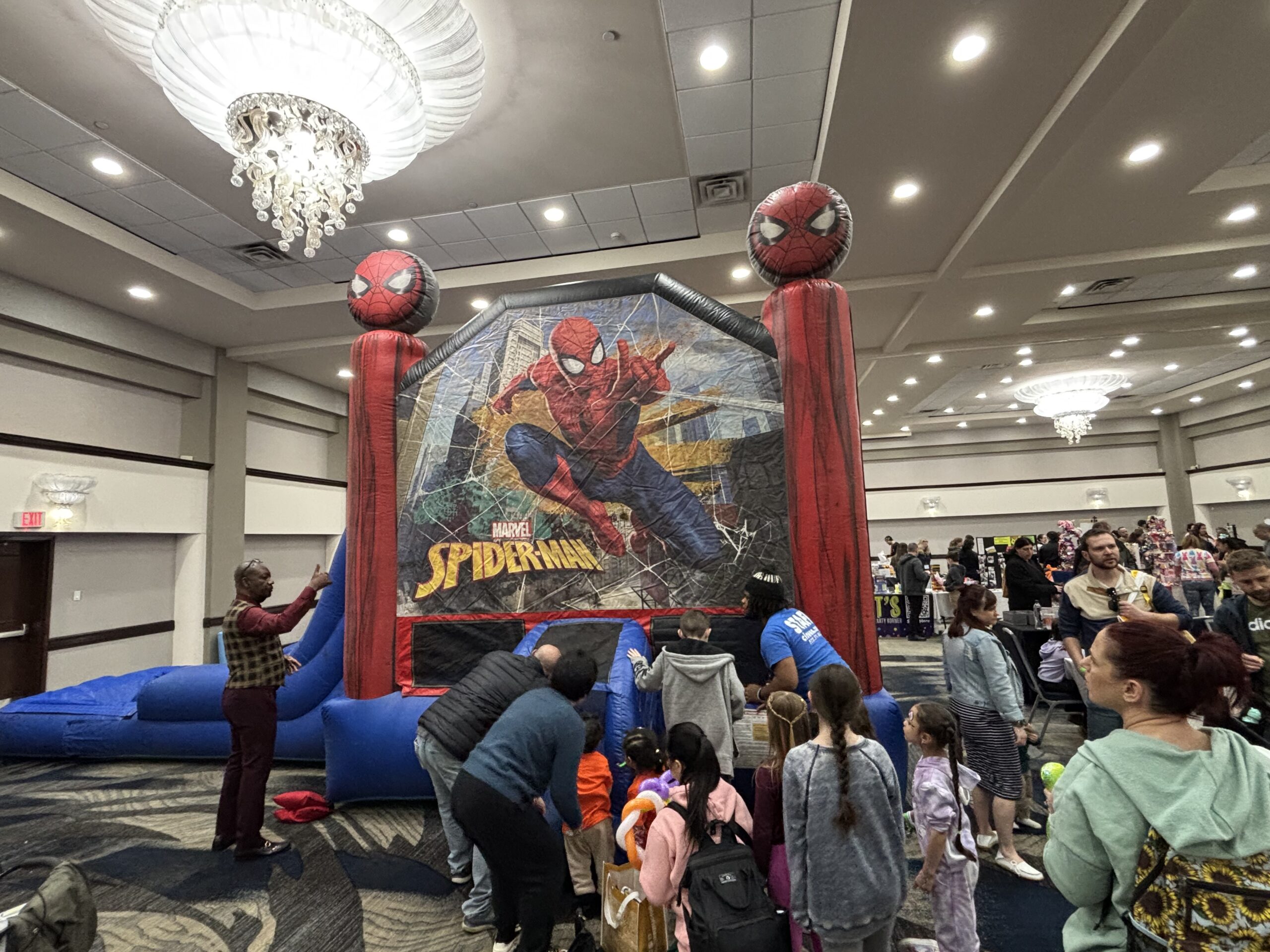 Many people stand next to the Spiderman bounce house
