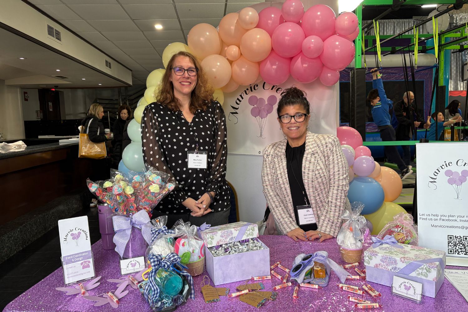 2 representatives at the booth of Marvic Creations. There is a pretty balloon arch behind them